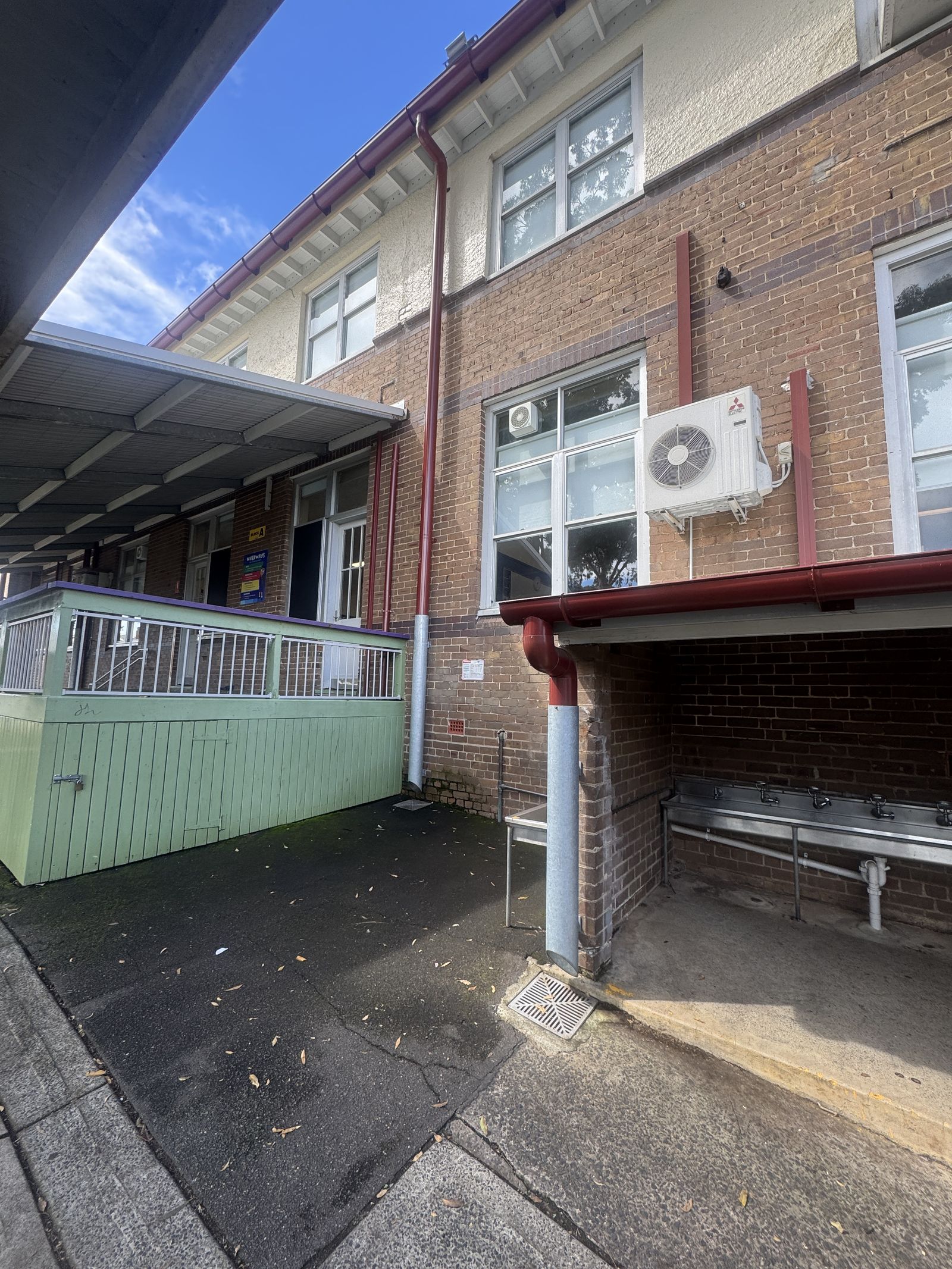 Two-storey brick building with red gutters and downpipes, a covered walkway and an outdoor sink area