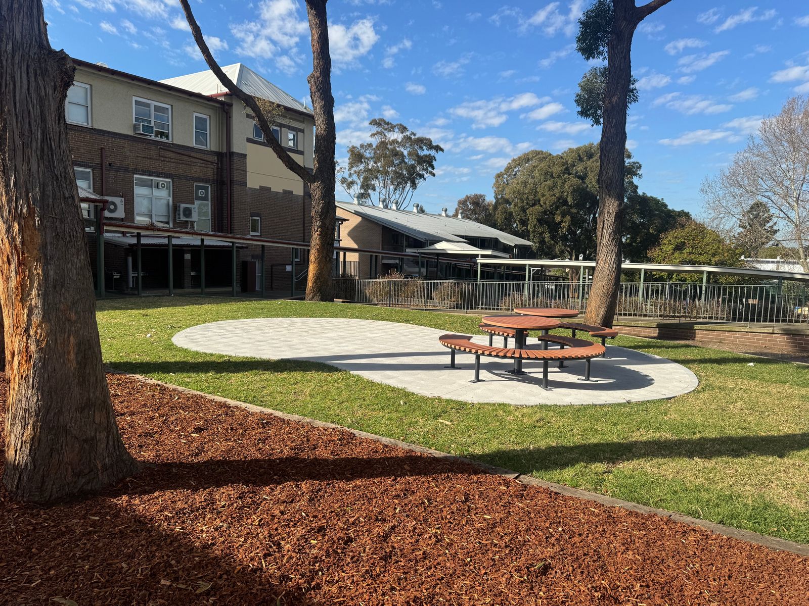 Curved timber bench seating on a concrete pad with new turf and freshly mulched garden beds in a courtyard